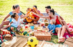 Multiracial families having fun together with kids at pic nic barbecue party - Joy and love life style concept with mixed race people toasting juices with children at park - Warm bright filter