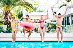 Front view of friends jumping in swimming pool with lilo airbed at luxury resort party - Life style vacation concept with happy guys and girls having fun games in summer day - Bright vivid filter
