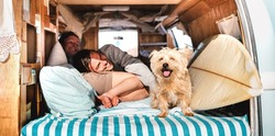 Hippie couple with cute pet traveling together on vintage retro campervan - Wanderlust and life inspiration concept with hippie lovers on mini van adventure journey on the road - Bright warm filter
