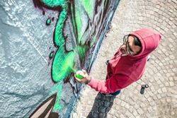 Top view of street artist painting graffiti on generic wall - Modern art concept with urban guy performing and preparing live murales with green aerosol color spray - Bright vivid filter