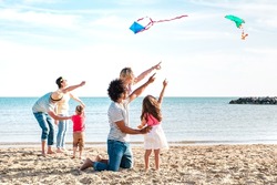 Multiple mixed families composed by parents and children playing with kite at beach vacation - Summer joy life style concept with candid people having fun together at seaside - Bright vivid filter
