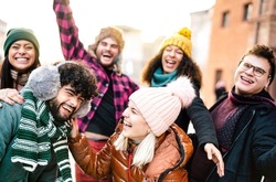 International guys and girls taking funny face selfie wearing warm fashion clothes - Happy life style concept with milenial people having fun together outside on winter holidays - Warm sunshine filter