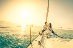 Young couple in love on sail boat with champagne at sunset - Happy exclusive alternative lifestyle concept  - Soft focus due to backlight on vintage nostalgic filter - Fisheye lens and tilted horizon