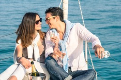 Young couple in love on sail boat with champagne flute glasses - Happy exclusive alternative lifestyle concept - Boyfriend and girlfriend flirting on luxury sailboat - Sunny afternoon color tones