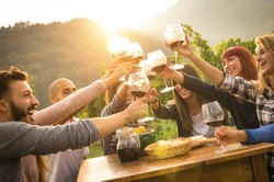 Happy friends having fun outdoor - Young people enjoying harvest time together outside at farm house vineyard countryside - Youth friendship concept - Hand toasting wine glass at winery on fall sunset