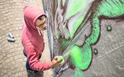 Street artist painting colorful graffiti on generic wall - Modern art concept with urban guy performing and preparing live murales with green aerosol color spray - Sunny afternoon neutral filter