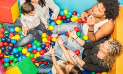 Happy multiracial mom and dad playing with daughter inside ball pit swimming pool with soap bubble blower - Multicultural family concept with happy children having fun with parents at kid toyroom