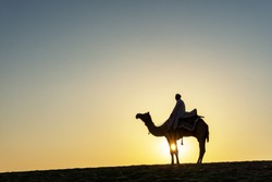 Silhouette of Indian man and camel during sunrise at Thar desert in Jaisalmer, Rajasthan, India.