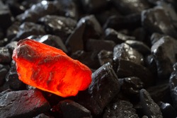 Red hot coal nugget on focus on other cold raw nuggets of coal. Background of raw coals with soft focus exclusion with color and temperature.
