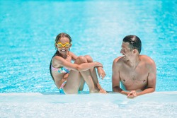 Family enjoying summer vacation in luxury swimming pool. Father and daughter splashing and having fun