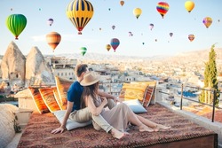 Happy couple on a rooftop in Cappadocia with hot air balloons in the background. Hot air balloon flights in Turkey
