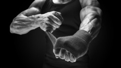 Close-up black and white photo of strong male hands Man is wrapping hands with boxing wraps isolated on black background Strong hands and fist, ready for training and active exercise