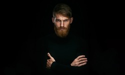 Hipster young man with folded and crossing hands standing Isolated on black background and looking at camera Hairstyle concept
