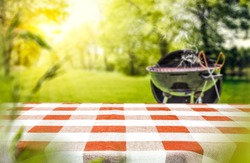 Red and white tableclothe in garden of free space for your decoration. Grill with smoke on grass. 