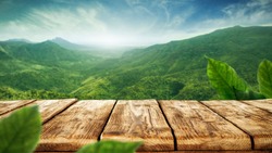 table background of free space for your decoration and blurred landscape of mountains.Blue sky with sun light and green small leaves. 