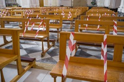 Christian church during the coronavirus pandemic Covid-19. Line strip or warning tape mark empty seats as new social distancing protection measures during pandemic of coronavirus in Italy.