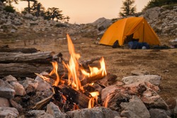 Bonfire burning in tourist camp in mountains. Beautiful campfire, burning wood by tent in summer evening. Active lifestyle, traveling, hiking and camping concept. Campfire burning in slow motion