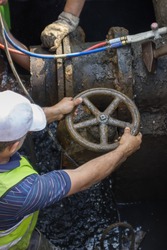 Industrial worker turning a valve on a large pipe, fixing broken water main. Selective focus.