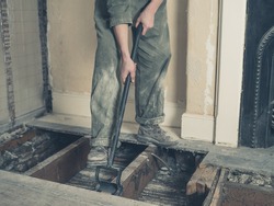 A young woman wearing a boiler suit is taken up the floor boards in a Victorian house
