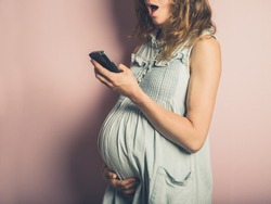 A surprised young pregnant woman is using her cell phone