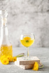 Dandelion homemade wine in a glass and bottle. Spring alcoholic drink. Light background.