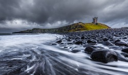 Long exposure of the sea and basalt rocks on the Northumberland coastline with Dunstanburgh Castle in background