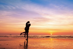 Couple kissing on the beach with a beautiful sunset in background, man lifting the woman