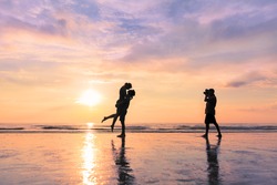 Photographer taking photo of a couple kissing on the beach during sunset - concept about romantic travels and honeymoon