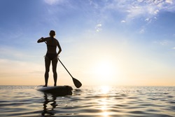 Girl stand up paddle boarding (sup) on quiet sea at sunset