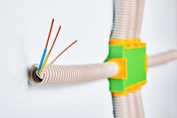The conduit is connected to the electrical distribution box of the household wiring, the ends of the bare copper wires are visible from the outside of the pipe. Installation of a electric panel.
