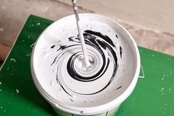 House painter mixes two paints using mixer for bucket with paddle mixing tool.