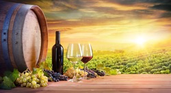 Wine Glasses And Bottle With Barrel In Vineyard At Sunset
