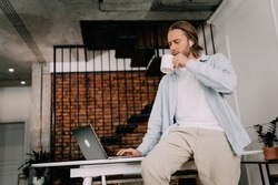 Man drinks coffee at the workplace In a stylish office or coworking space, an employee chills with a cup of tea