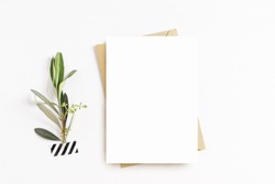 Feminine stationery, desktop mock-up scene. Blank greeting card, craft envelope, washi tape and with olive branch.White table background. Flat lay, top view. 