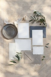 Summer wedding stationery mock-up scene. Blank greeting cards, envelopes, silver plate, silk ribbon and olive branches in sunlight. Marble background with shadows. Vertical feminine flat lay, top view