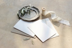 Closeup of summer wedding stationery mock-up scene. Blank greeting cards, envelopes, vintage silver plate with olive branch and silk ribbon. Marble background in sunlight, shadows. Top view.