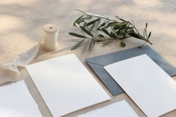 Closeup of summer wedding stationery mock-up scene. Blank greeting cards, invitations, envelopes, olive branch and silk ribbon. Marble background in sunlight, shadows. Top view.