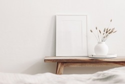 White frame mockup on vintage wooden bench, table. Modern white ceramic vase with dry Lagurus ovatus grass and marble tray. Blurred beige linen blanket in front, Scandinavian interior.