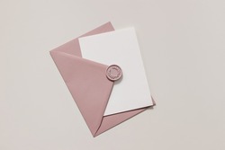Blank wedding greeting card, invitation mockup scene in sunlight. Closeup of pink envelope with decorative wax seal on table. Birthday stationery template. Flat lay, top view. Feminine composition.