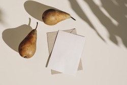 Summer still life composition. Autumn weddding greeting card, envelope mock up scene. Two pears fruit, long harsh shadows overlay. Beige table background in sunlight. Flat lay, top view, no people.