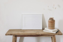 Summer, fall still life photo. Vase with dry lagurus, bunny tail grass in ceramic vase. Old wooden bench. Blank horizontal white picture frame mockup. White wall background. Empty copy space. Interior