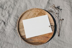 Blank greeting card card mockup on wooden plate, tray. Dry grass, plant in sunlight. Beige linen background, shadow overlay. Modern template for branding identity. Autumn, winter design. Flat lay, top