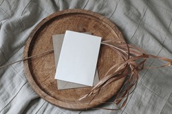 Boho wedding invitation. Blank greeting card mockup on wooden tray. Dry palm leaf. Beige cotton muslin throw, blanket. Tropical summer stationery template, design.  Flat lay, top view, no people.