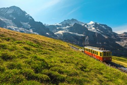 Cogwheel railway with retro electric red tourist train. Snowy Jungfrau mountains and red passenger train on the Jungfraujoch, Kleine Scheidegg, Grindelwald, Bernese Oberland, Switzerland, Europe