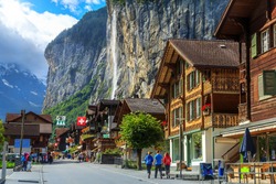Spectacular principal street of Lauterbrunnen with shops,hotels,terraces,swiss flags and stunning Staubbach waterfall in background,Bernese Oberland,Switzerland,Europe