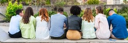 Multi ethnic young people sitting on a bench in a park from behind - shot from behind their backs - Wait concept – group person from back side – look from behind – rear view -  view of people behind p