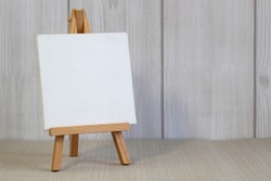 White canvas on a small easel on a light wooden background, close up, blank sheet concept with copy space