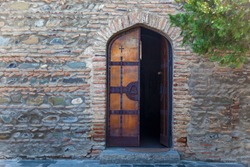 A half open wooden door of the church against the backdrop of a stone wall. Wooden doors of the church.