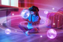 Child girl wearing virtual reality headset and looking at digital space system with planets or Universes. Space exploration with augmented reality glasses. She is sitting on flor at childroom.