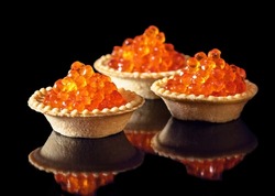 Red caviar in three tartlets over black background. Close-up salmon caviar. Delicatessen. Gourmet food. Texture of caviar. Seafood